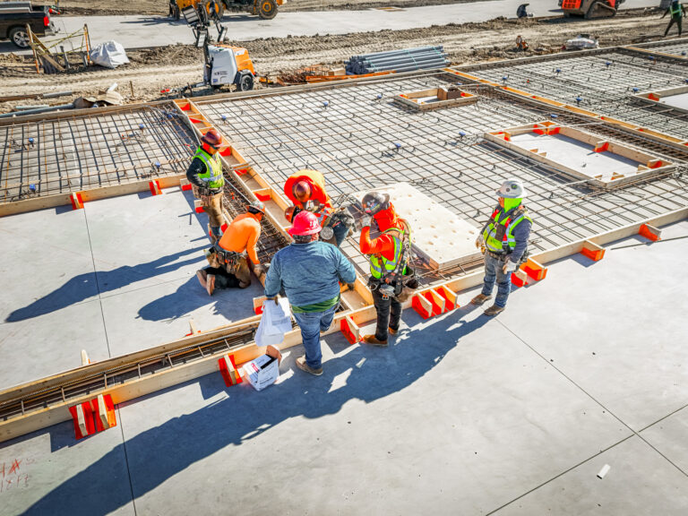Crews placing rebar inside orange formwork to cast tilt-wall panels on the floor slab at a Reliable Commercial job site in Dallas-Fort Worth